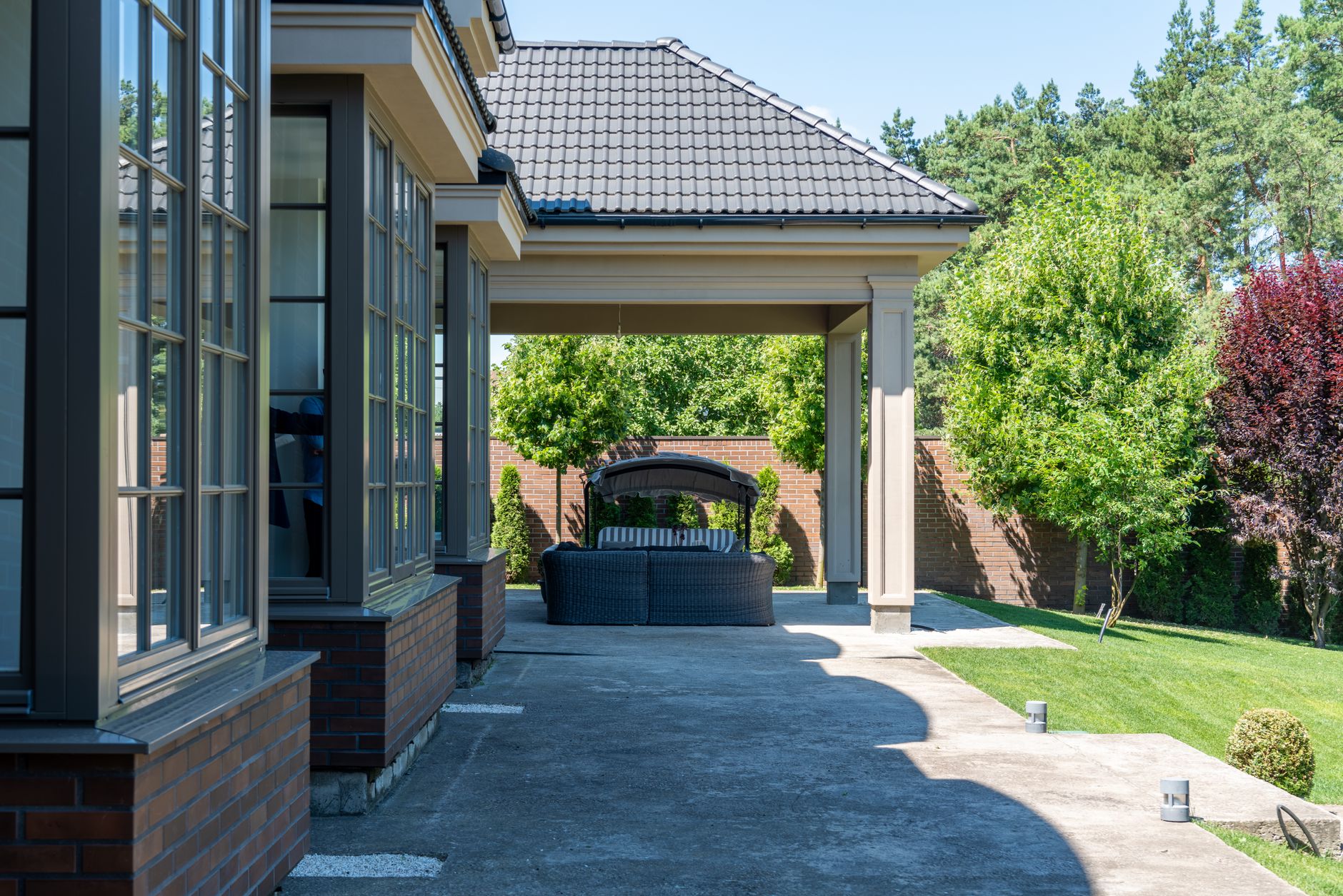 Relaxing patio with modern furniture, garden view, and tiled roof in a summer setting.